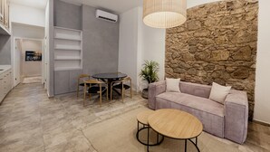 A modern living room with a stone accent wall, a gray sofa, a round table, and a dining area with chairs. - Unique Apartment with Jacuzzi (Ciudad de Panamá)