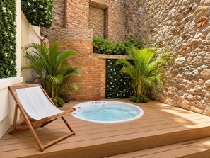 Una terraza de madera con un jacuzzi, rodeada de plantas y un muro de piedra.