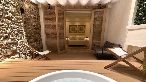 A hot tub in a wooden deck area with a stone wall and a sofa in the background. - Unique Apartment with Jacuzzi (Ciudad de Panamá)