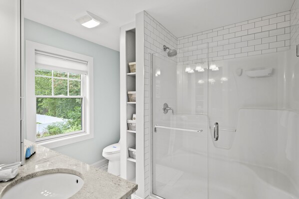 Een moderne badkamer met een glazen douchecabine, toilet en een raam met uitzicht op groen.