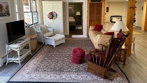 A cozy living room with a television, wicker furniture, a patterned rug, and a wooden chair. - The Cozy Pine, where your Grand Marais Retreat Begins! (Grand Marais)