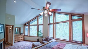 A bedroom with a large bed, a ceiling fan, a dresser, and a window with a view of trees. - Game room, Complete Retreat, Stonehaven (Morgantown)