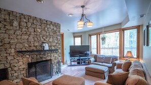 A living room with a stone fireplace, a flat-screen TV, and a large window overlooking a deck. - Game room, Complete Retreat, Stonehaven (Morgantown)