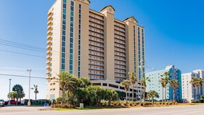 A multi-story hotel with balconies, a parking lot, and palm trees.