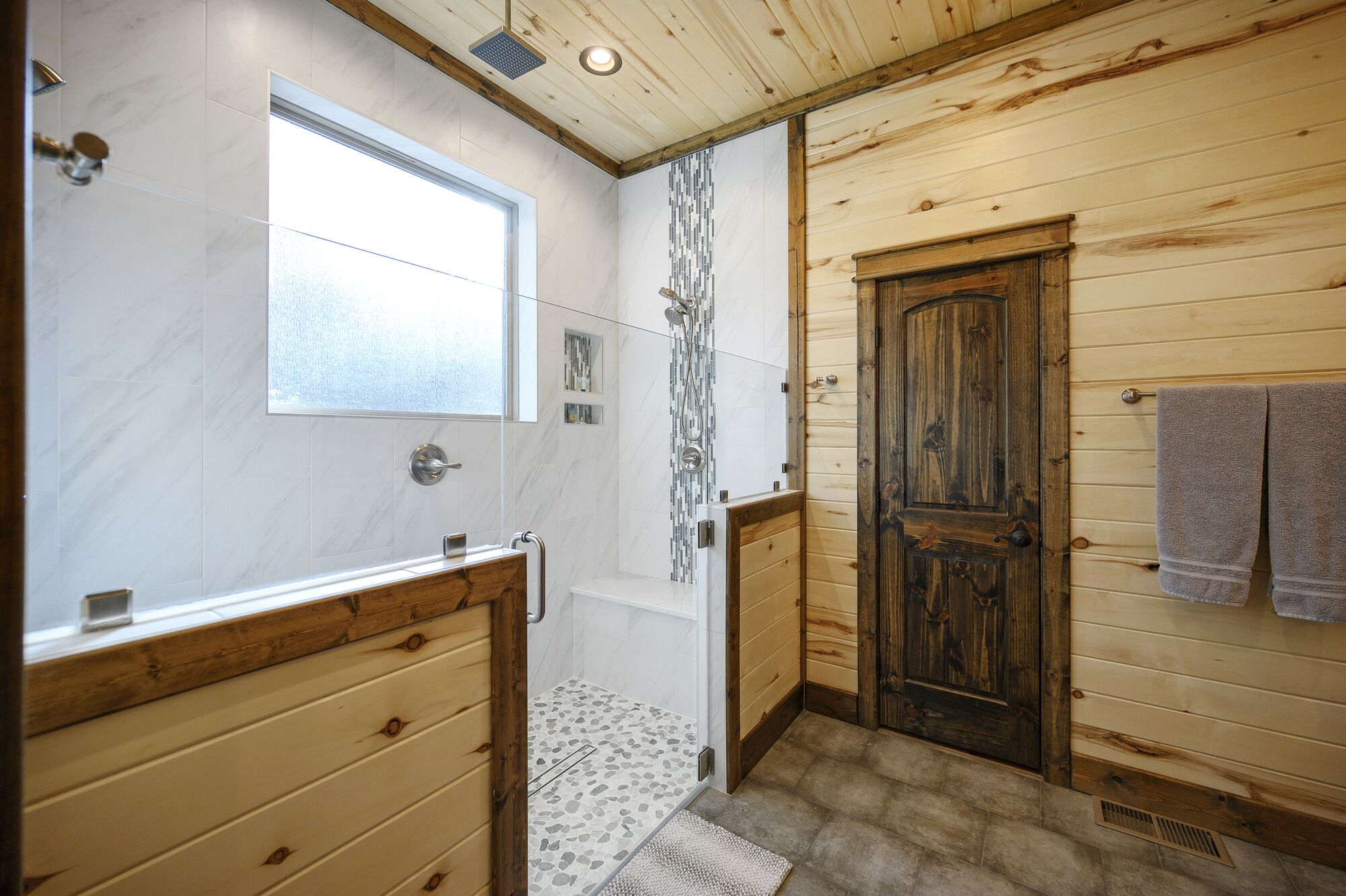 A bathroom with a wooden door, a shower with a glass enclosure, and a vanity with a mirror.