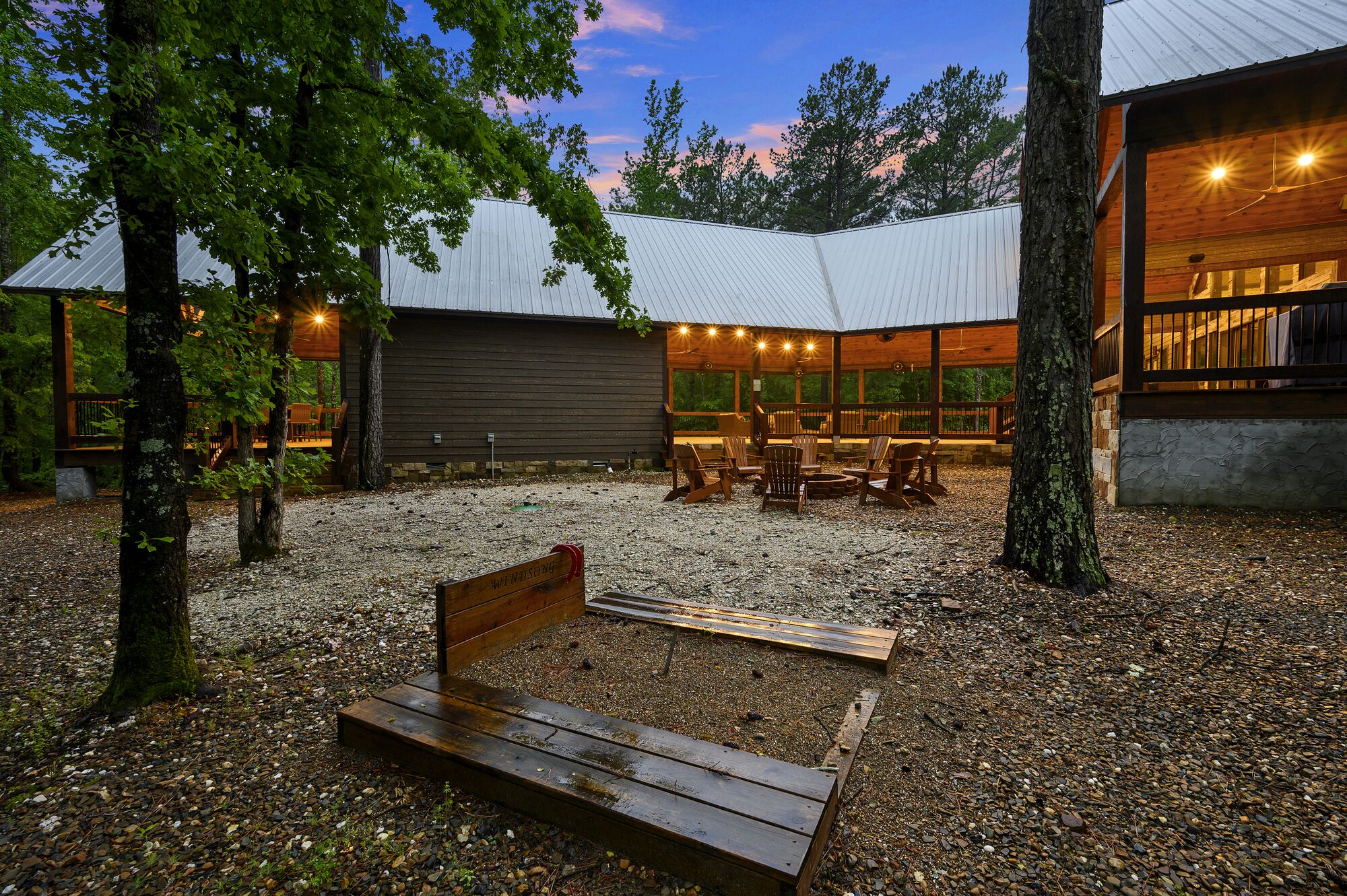 Eine Holzdielen-Terrasse mit einer Bank, umgeben von Bäumen und einem Kiesweg.