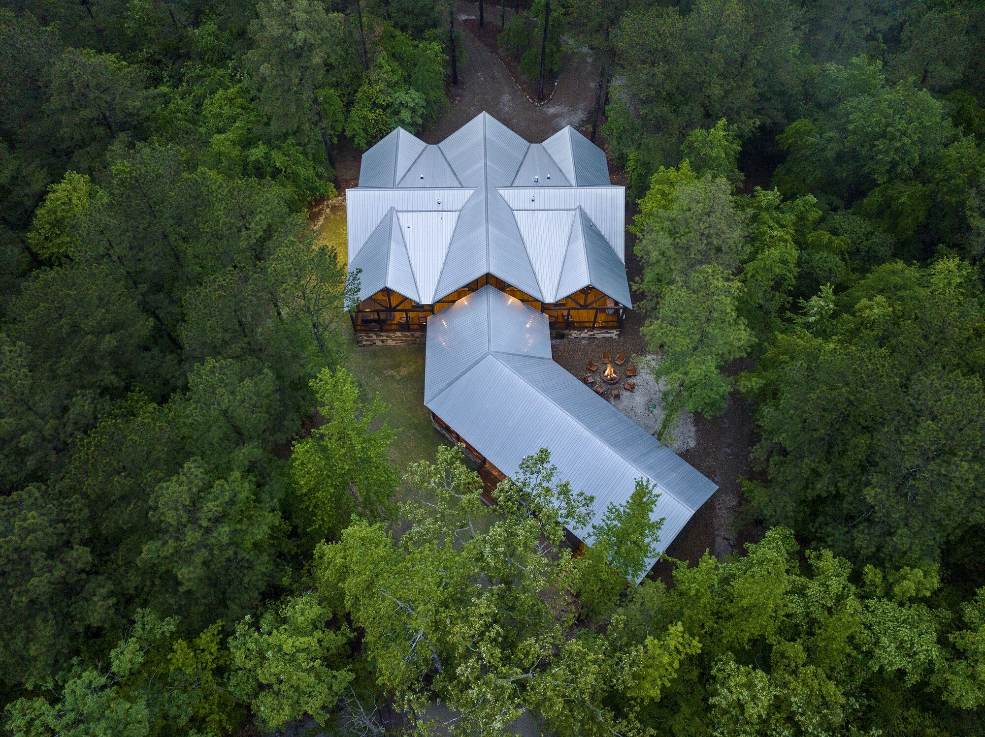 Uma pousada moderna com estrutura de telhado geométrica única, rodeada por uma floresta densa.