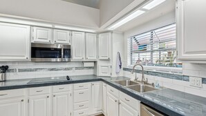 A modern kitchen with white cabinetry, a stainless steel microwave, and a large window with blinds. - 4 Bedroom Incredible Backyard with Pool! (Glendale)