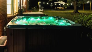A hot tub with green lights, surrounded by a backyard with a house, a tree, and outdoor lighting.