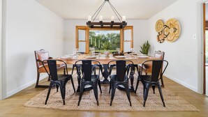 A dining room with a large wooden table, black chairs, and a chandelier.