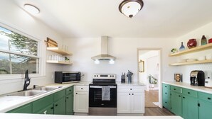 A modern kitchen with green cabinets, white countertops, a stainless steel oven, and a microwave.