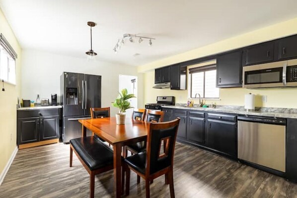Enjoy cooking in this well-equipped kitchen with a refrigerator, microwave, and dishwasher. A dining table for four and a potted plant add a touch of warmth.