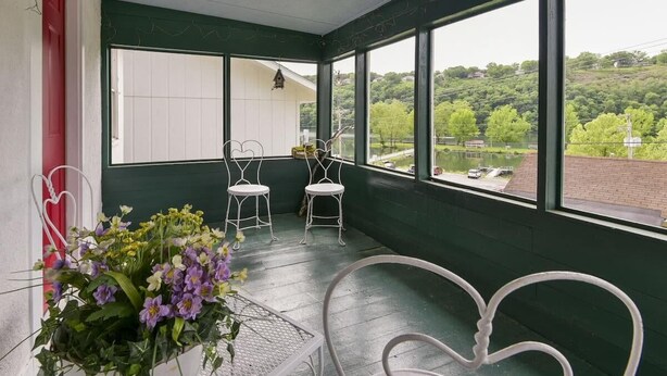 A covered porch with two white chairs, a potted plant, and a view of a lake and greenery. - Historic Water's Edge Cottage 6 (Rockaway Beach)