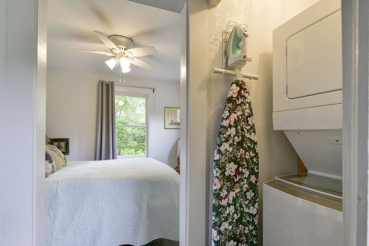 A bedroom with a bed, a ceiling fan, a window with curtains, and a washing machine.