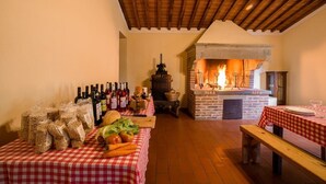 Une pièce rustique avec une cheminée en briques, des poutres en bois et une table recouverte d’une nappe à carreaux, sur laquelle sont disposés de la nourriture et des bouteilles de vin.