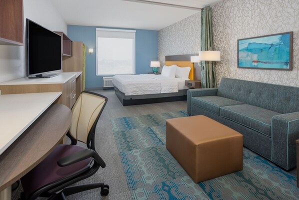 Habitación de hotel con cama, sofá, escritorio con televisor, silla y piso alfombrado.