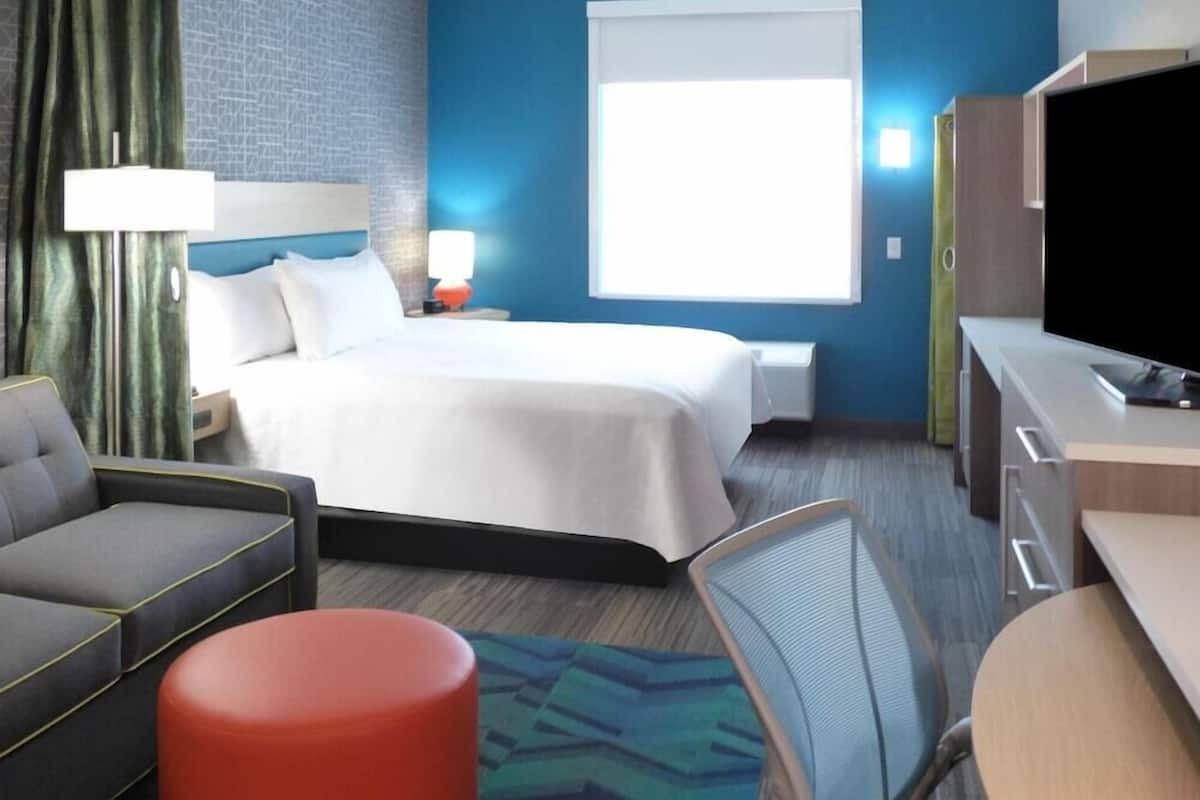 A hotel room with a bed, a desk, a chair, a sofa, and a television.