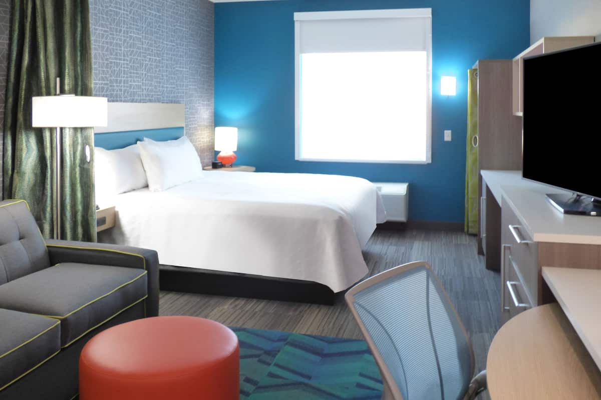A hotel room with a bed, a desk, a chair, a sofa, and a TV.