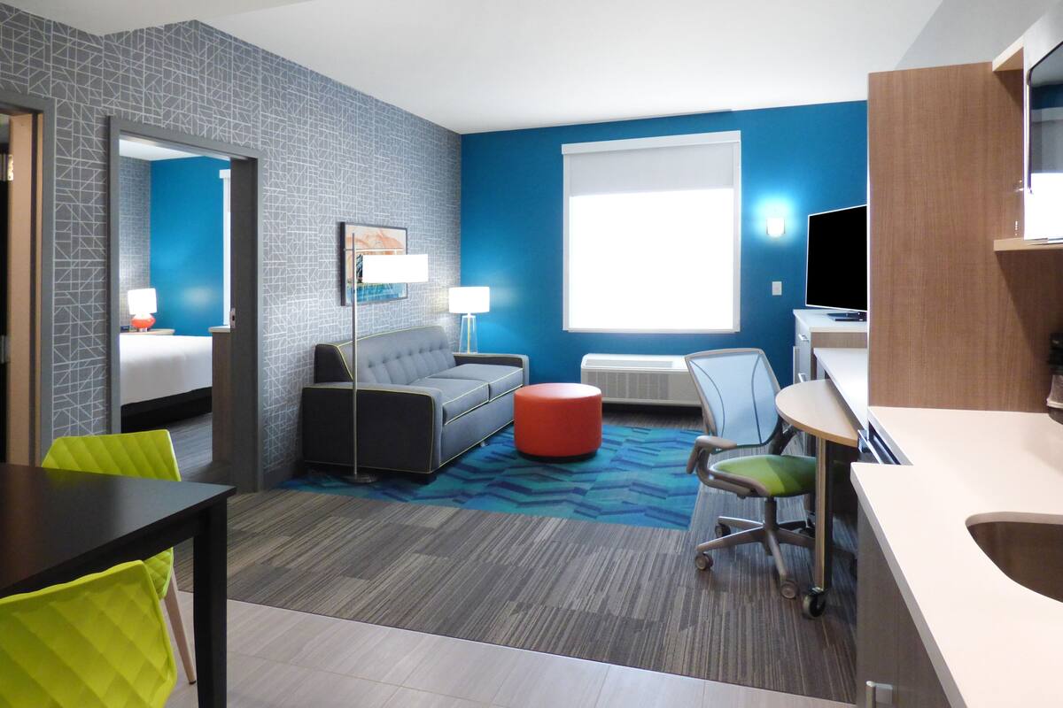 A hotel room with a bed, a sofa, a desk, a chair, and a TV.