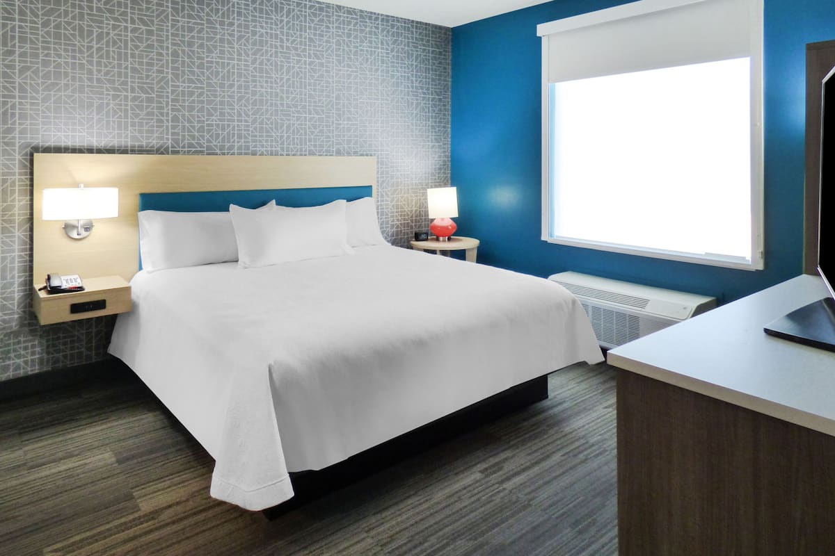 A hotel room with a bed, two bedside tables, a desk, a window, and a wall with a geometric pattern.