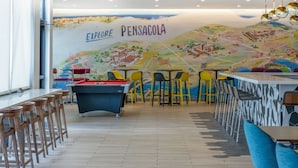 Ein Billardraum mit Pooltisch, Holzbarhocker und einem Wandgemälde mit dem Titel 'EXPLORE PENSACOLA'.