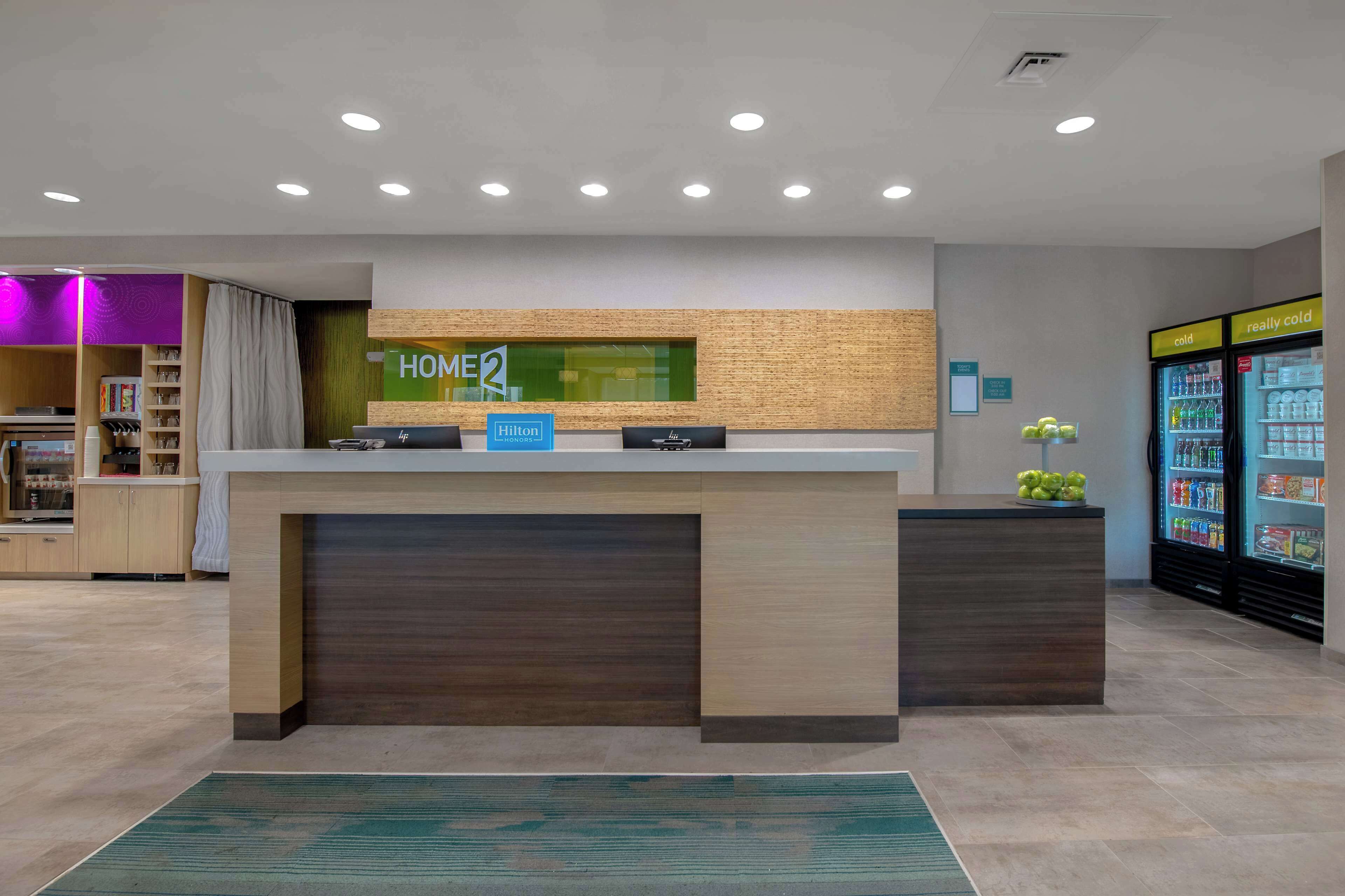 Een hotel receptiebalie met een 'HOME2' bord, een 'Hilton' bord en een drankkoelkast.