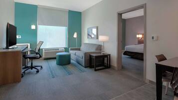 Habitación de hotel con escritorio, silla, sofá, reposapiés, lámpara y cama.