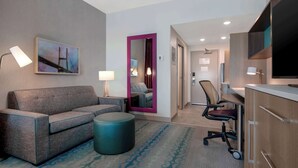 Habitación de hotel con sofá, reposapiés, escritorio, silla y un espejo grande con marco rosa.