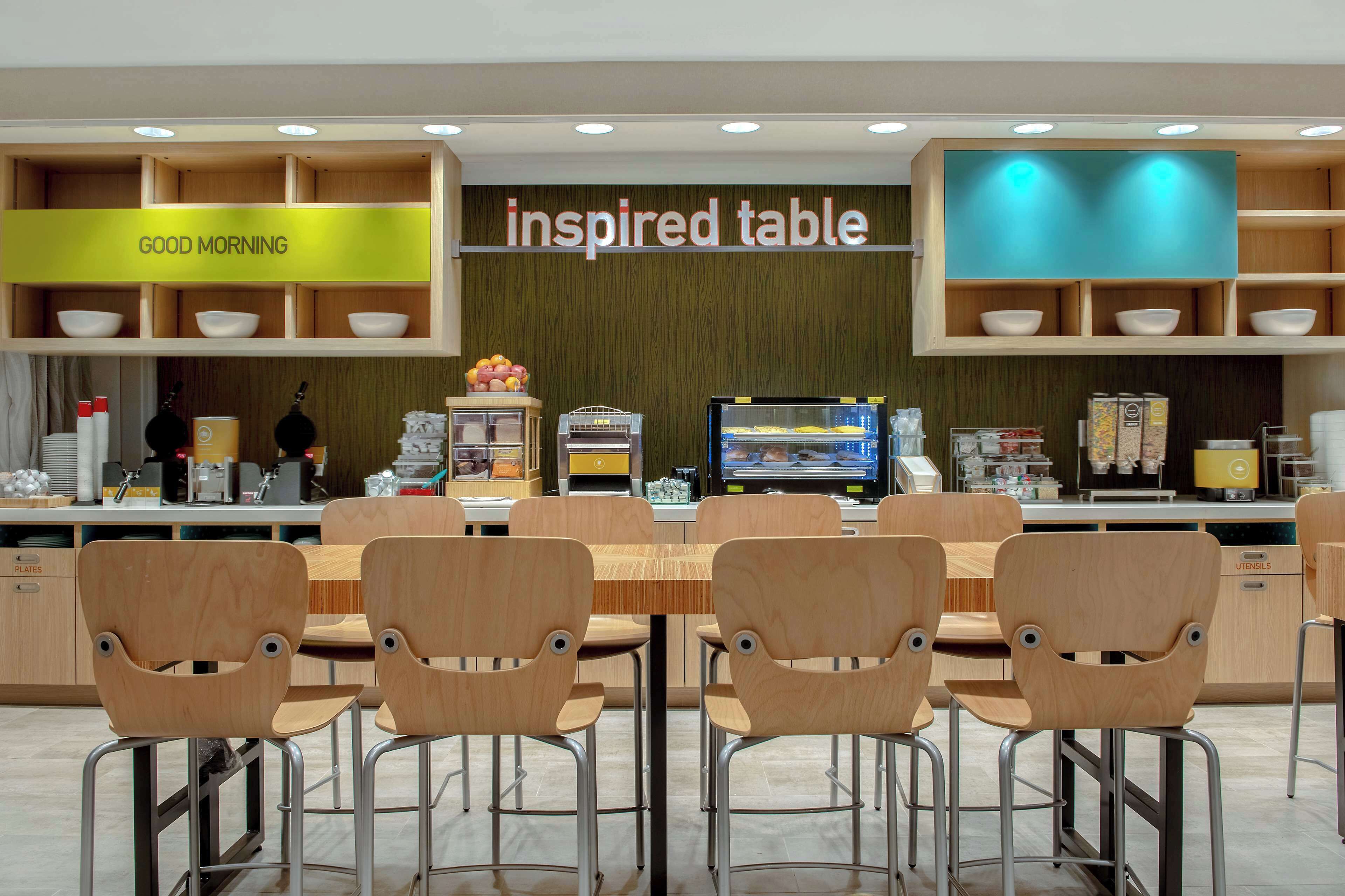 Um café moderno com mesa e cadeiras de madeira, uma máquina de café e um letreiro que diz 'inspired table'.