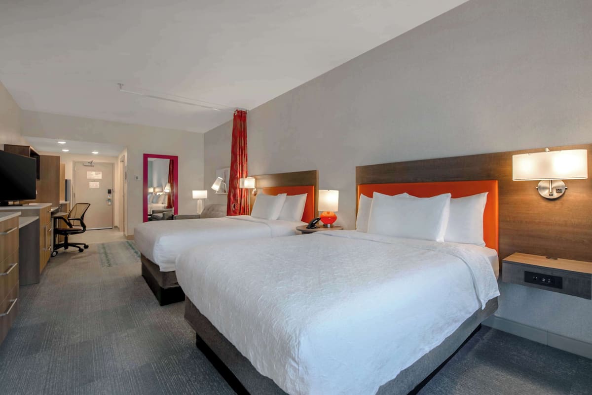 A hotel room with two beds, a desk, a chair, a TV, and a mirror.