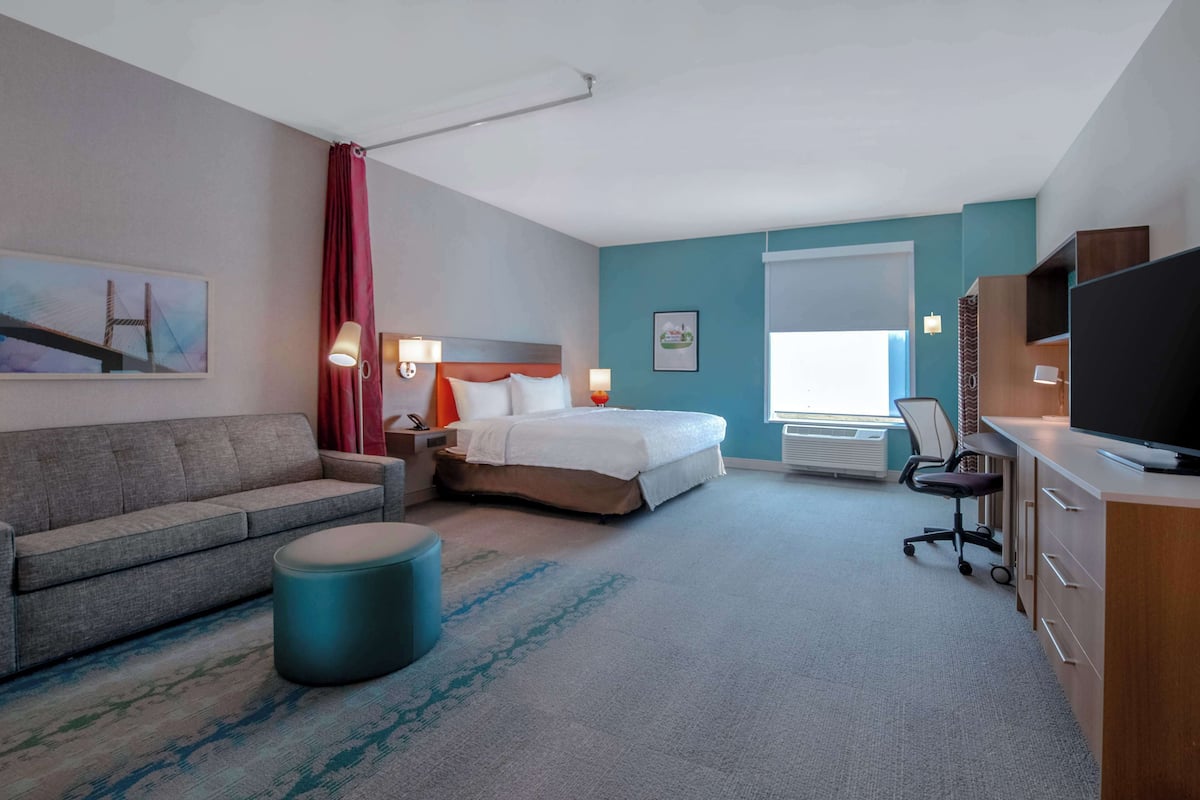 A hotel room with a bed, a sofa, a desk, a television, and a window.