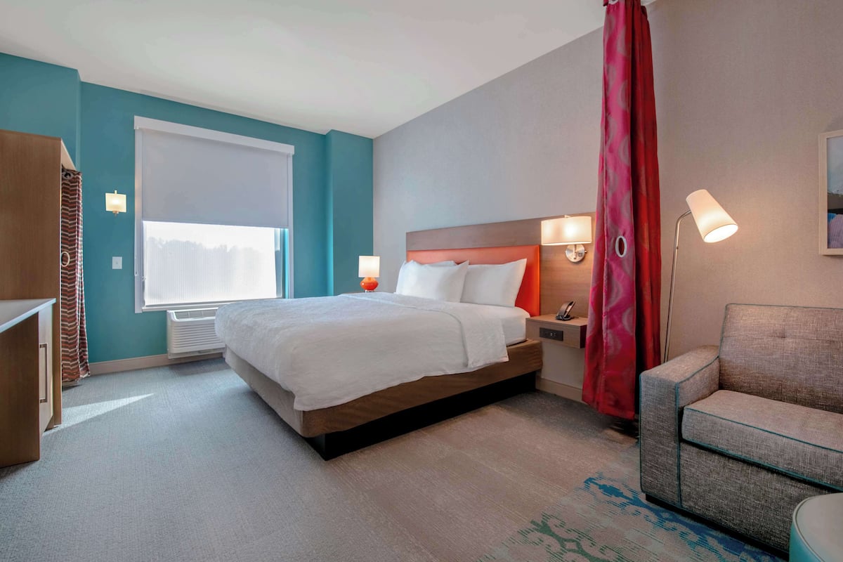 A hotel room with a bed, bedside lamps, a sofa, and a window with blinds.