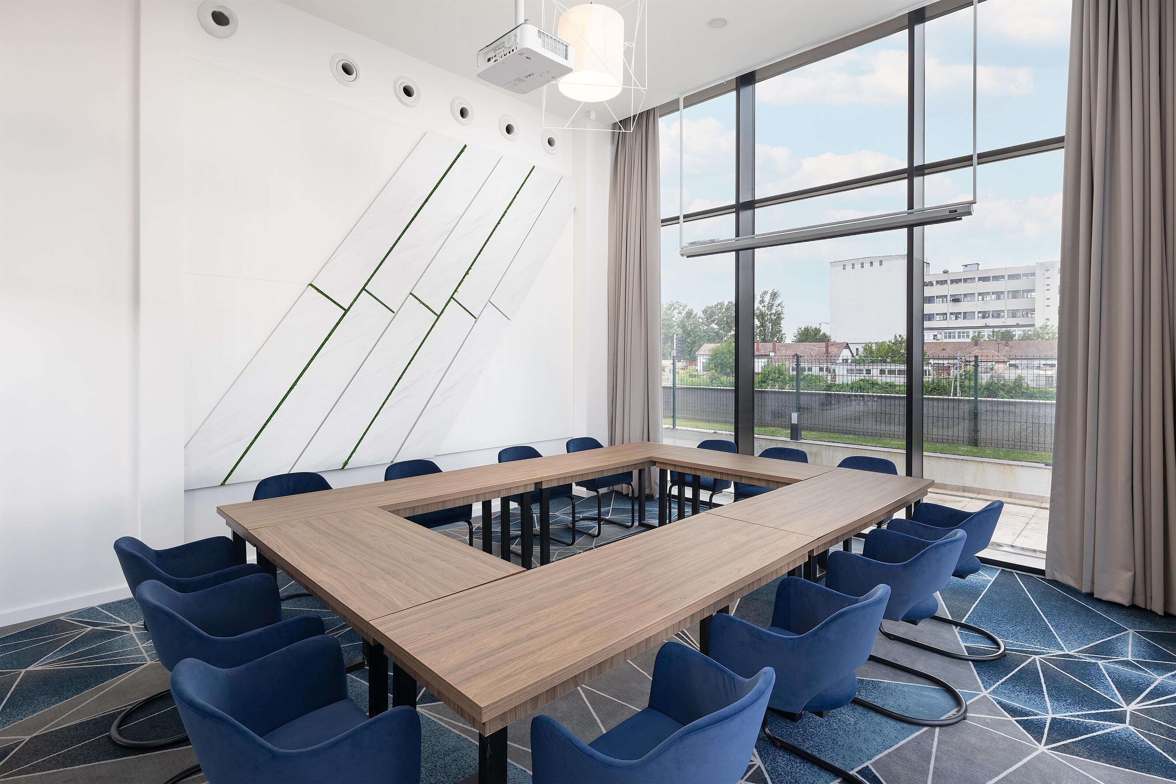 A conference room with a long table, blue chairs, and a large window with a view of buildings and greenery.