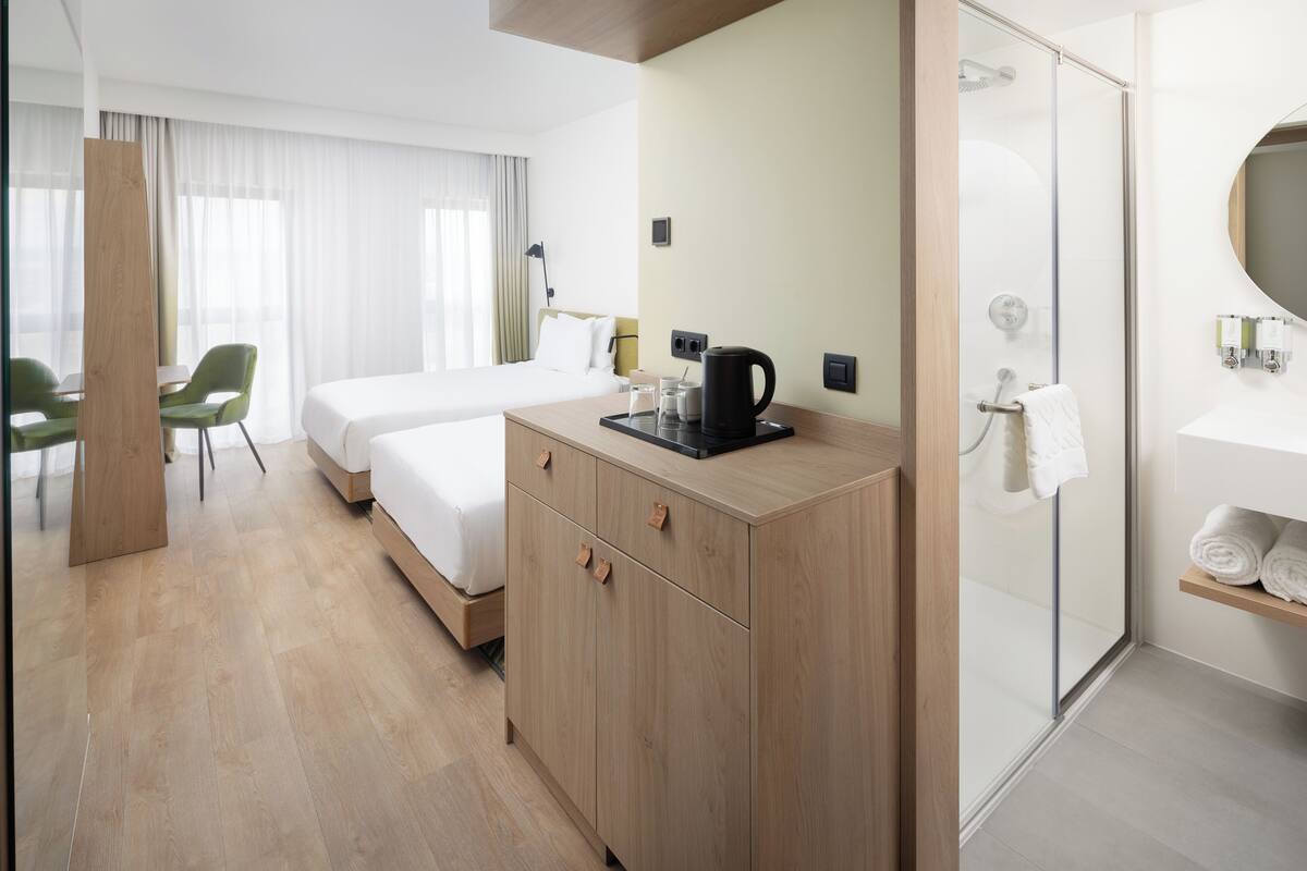 A hotel room with a bed, a desk, a coffee maker, a shower, and a bathroom with a mirror and towel rack.