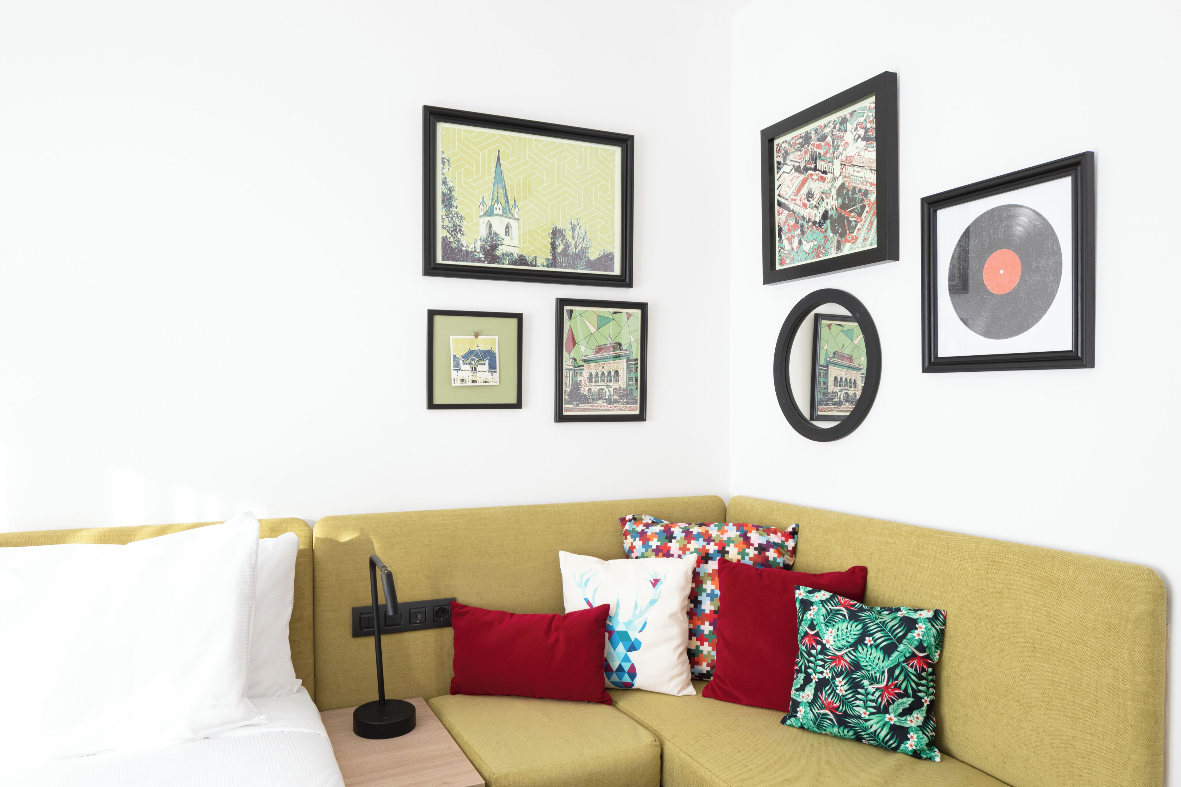 Une pièce avec un canapé jaune, de nombreux coussins et des tableaux encadrés accrochés au mur.