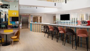 A modern bar area with a high ceiling, a flat-screen TV, and a variety of seating options including bar stools and a bench. - Hampton by Hilton Targu Mures (Targu Mures)