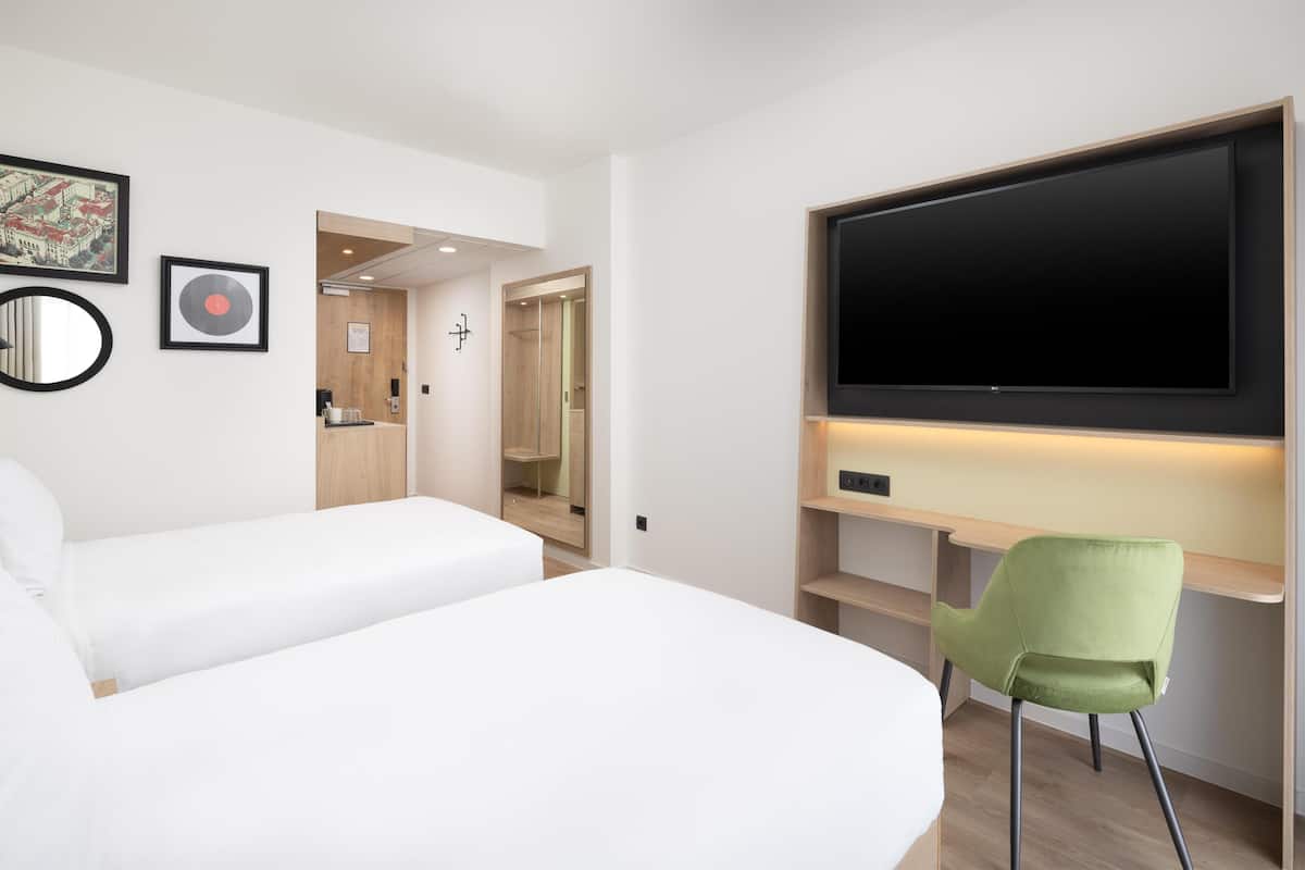 A modern hotel room with a large bed, a desk with a chair, a flat-screen TV, and a mirror.