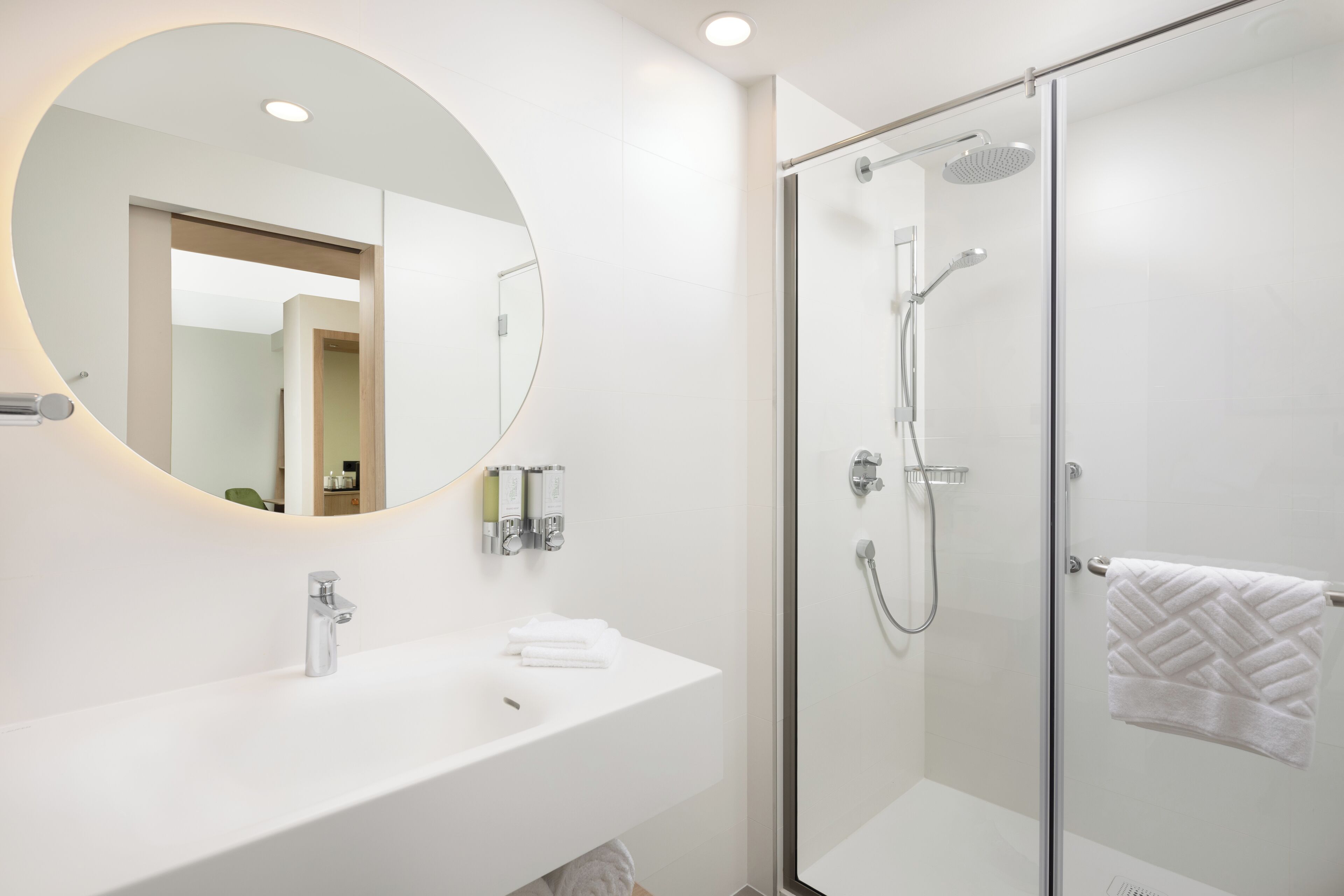 A modern bathroom with a round mirror, a white sink, and a glass-enclosed shower.