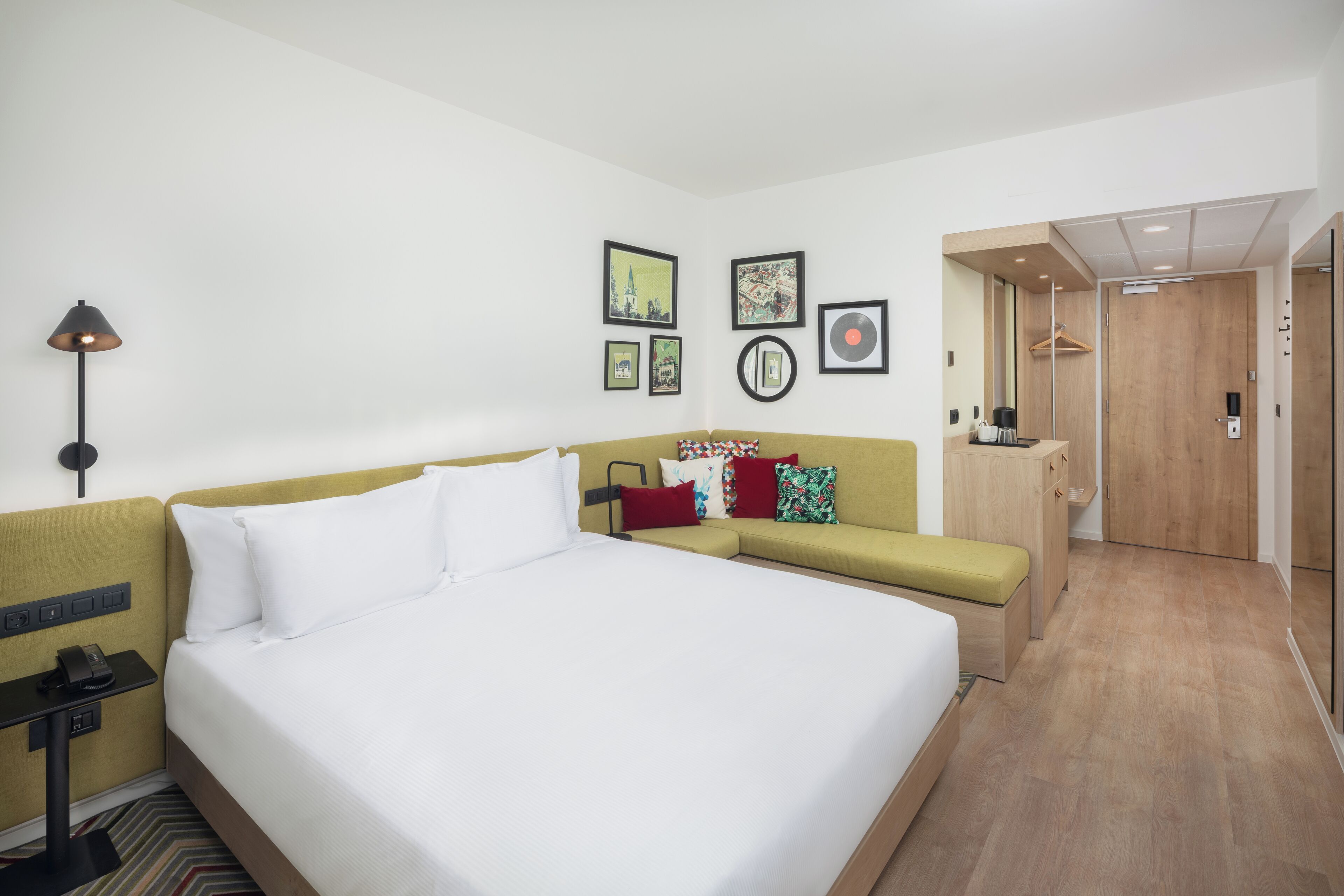 A hotel room with a large bed, a sofa, a desk with a lamp, and a wardrobe.