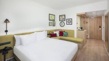 A hotel room with a large bed, a sofa, a desk with a lamp, and a wardrobe.