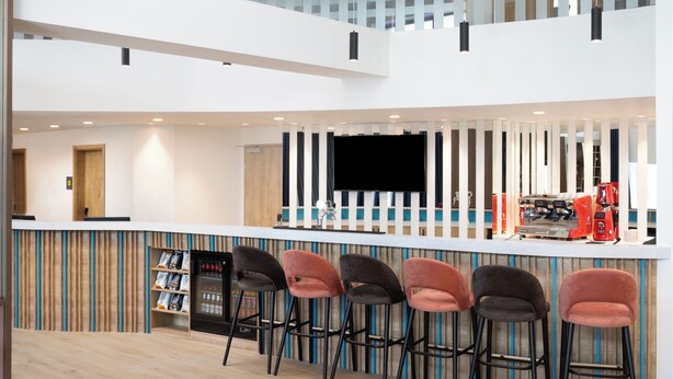 A modern bar area with a high ceiling, colorful light fixtures, and a bar counter with stools. - Hampton by Hilton Targu Mures (Targu Mures)