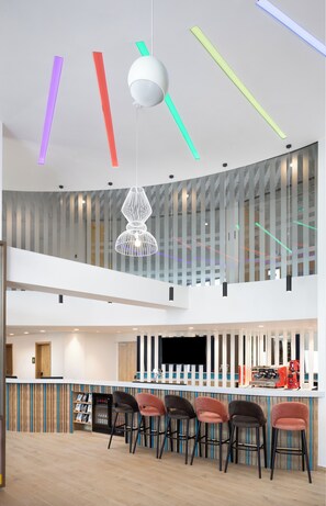 A modern bar area with a high ceiling, colorful light fixtures, and a bar counter with stools. - Hampton by Hilton Targu Mures (Targu Mures)