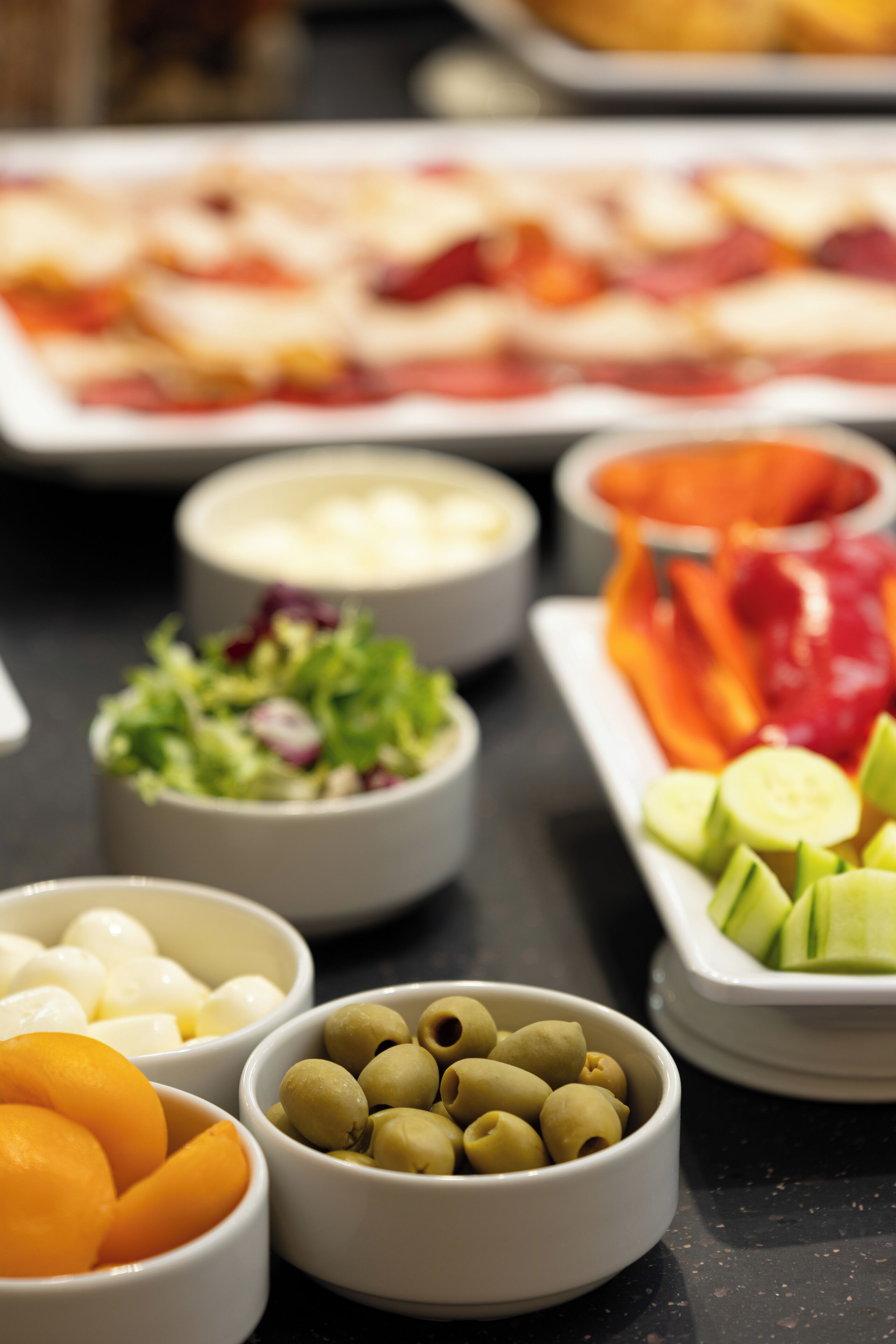 A table with various food items including olives, sliced cucumbers, and a salad.