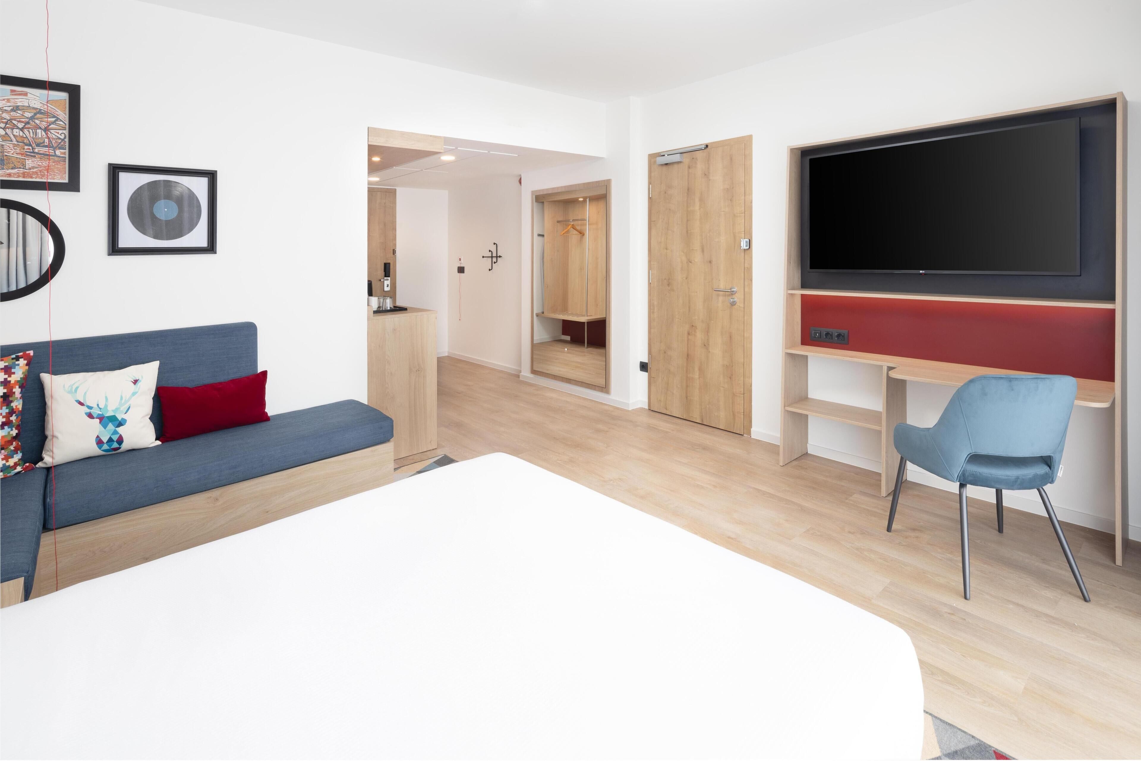 Une chambre d’hôtel moderne avec un grand lit, un canapé bleu, un bureau avec un téléviseur à écran plat et une armoire.