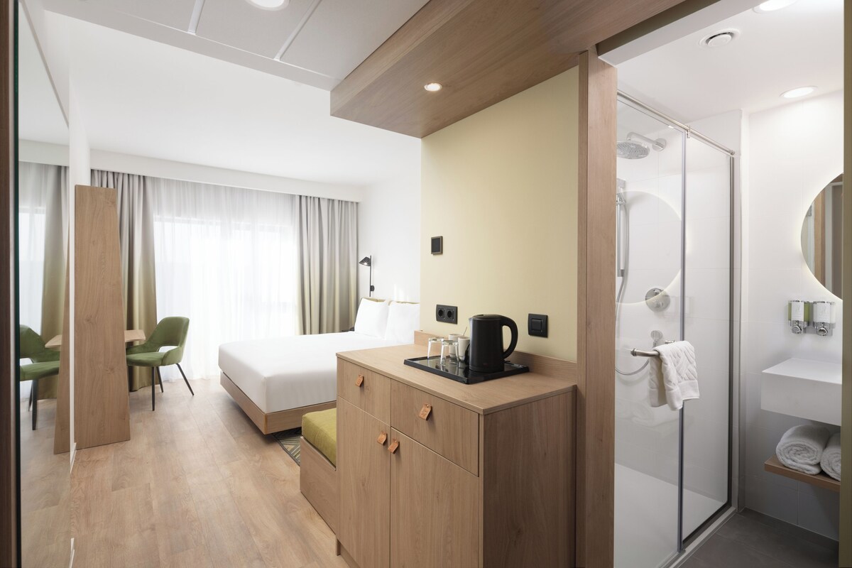 A hotel room with a bed, a wooden dresser, a shower, and a seating area with chairs.