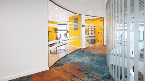 A modern office space with curved white walls, a colorful carpet, and a glass partition with yellow accents. - Hampton by Hilton Targu Mures (Targu Mures)