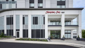 A modern Hampton Inn hotel with a curved facade, large windows, and a prominent entrance with a glass door.