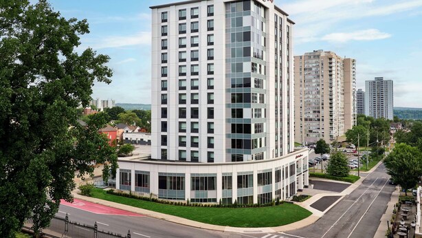 A modern hotel with a prominent 'Hampton Inn' sign, featuring a corner building with multiple floors and large windows.