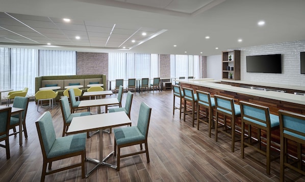 Un moderno vestíbulo de hotel con zona de bar, diferentes disposiciones de asientos y una amplia pantalla de televisión.
