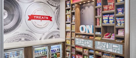 A snack and treat section with refrigerated vending machines, shelves stocked with various snacks, and a wall mural with the word "TREAT" prominently displayed.